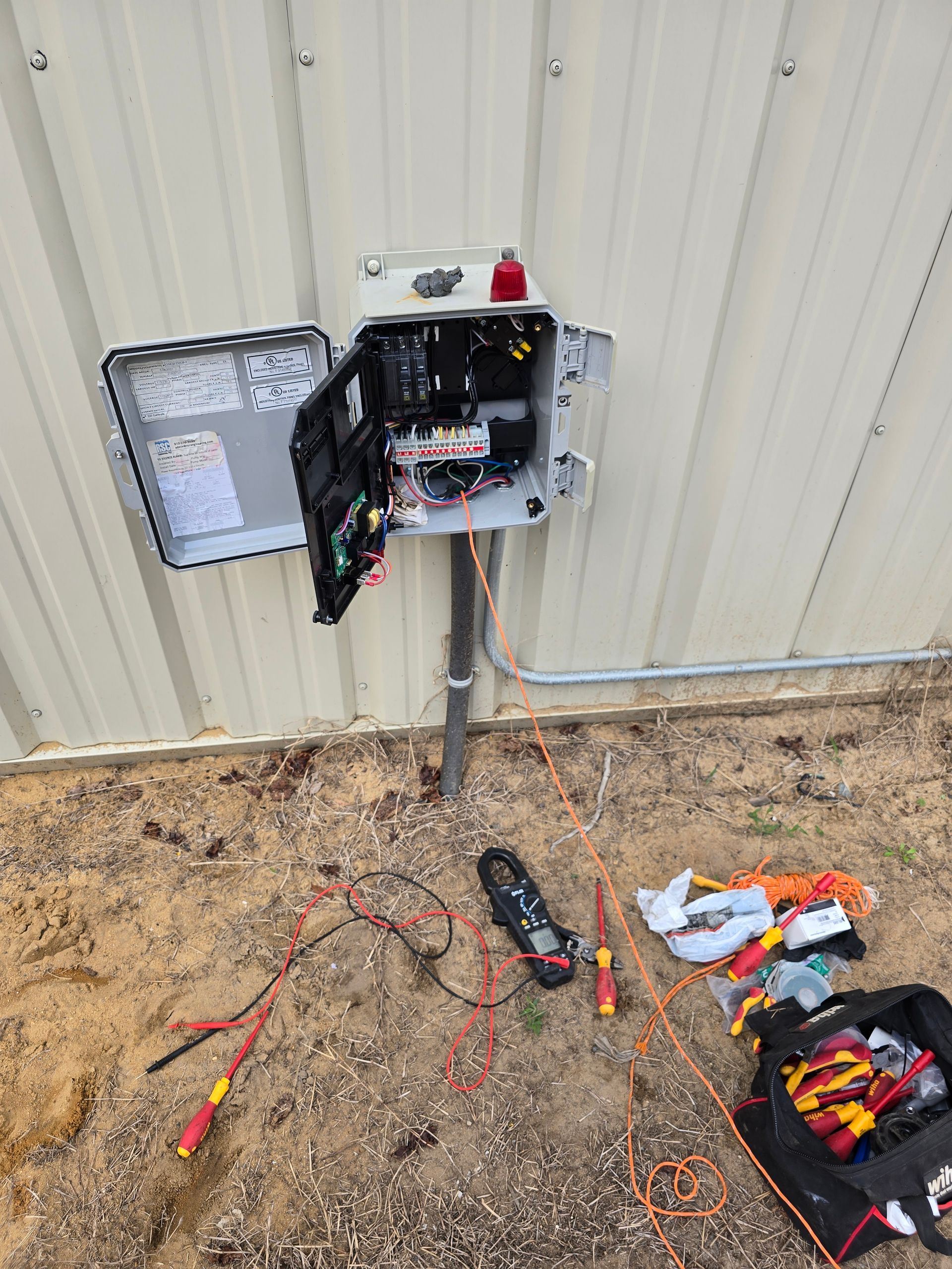 Open electrical box on a pole; tools and wires lie on the ground.