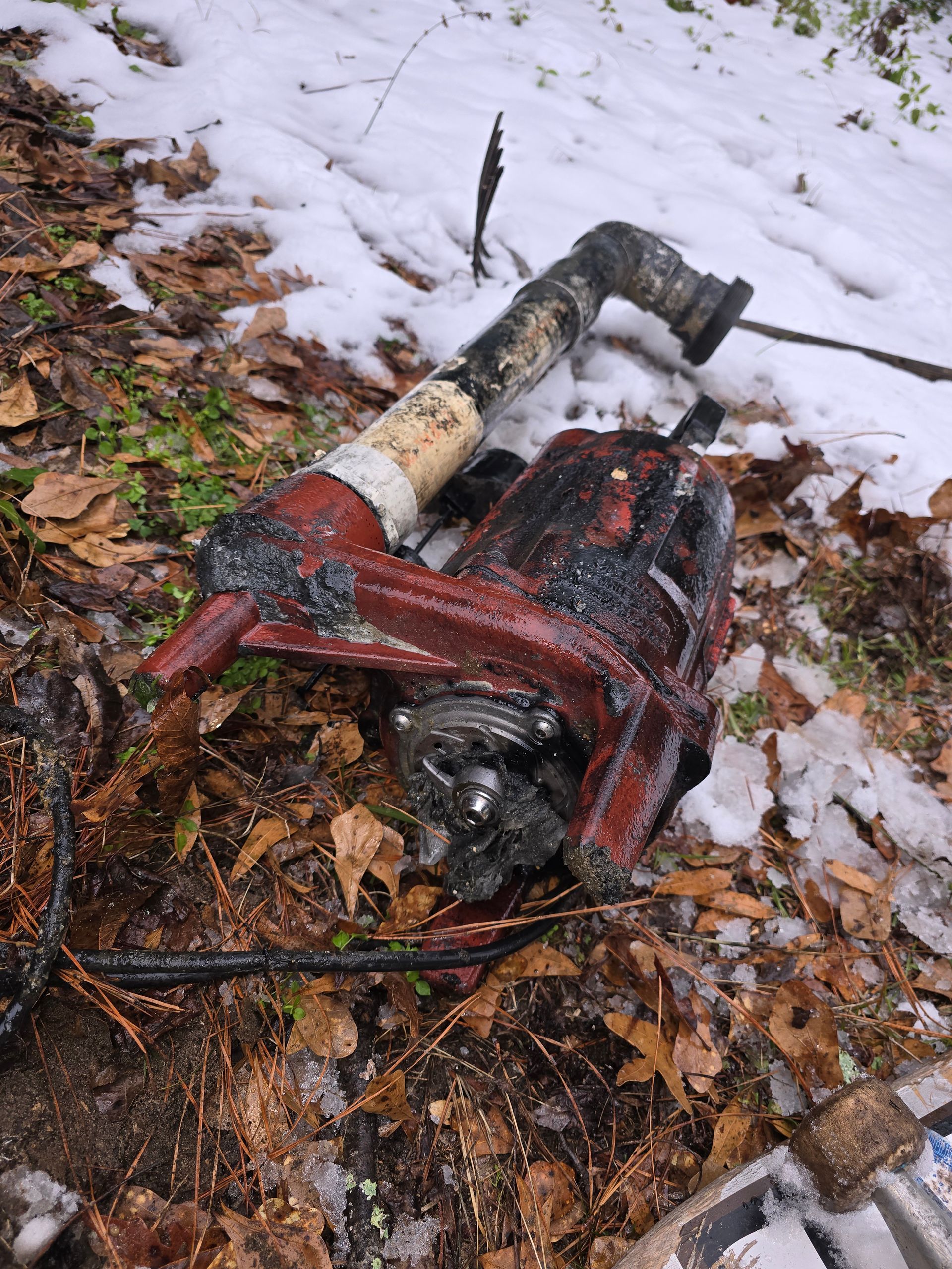 Red pump with black pipe in a snowy, wooded area.