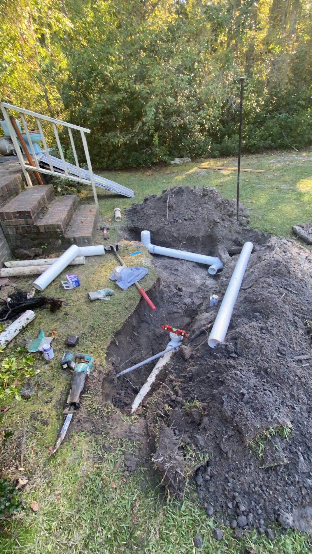Outdoor plumbing repair site with exposed pipes and dirt pile near a porch.