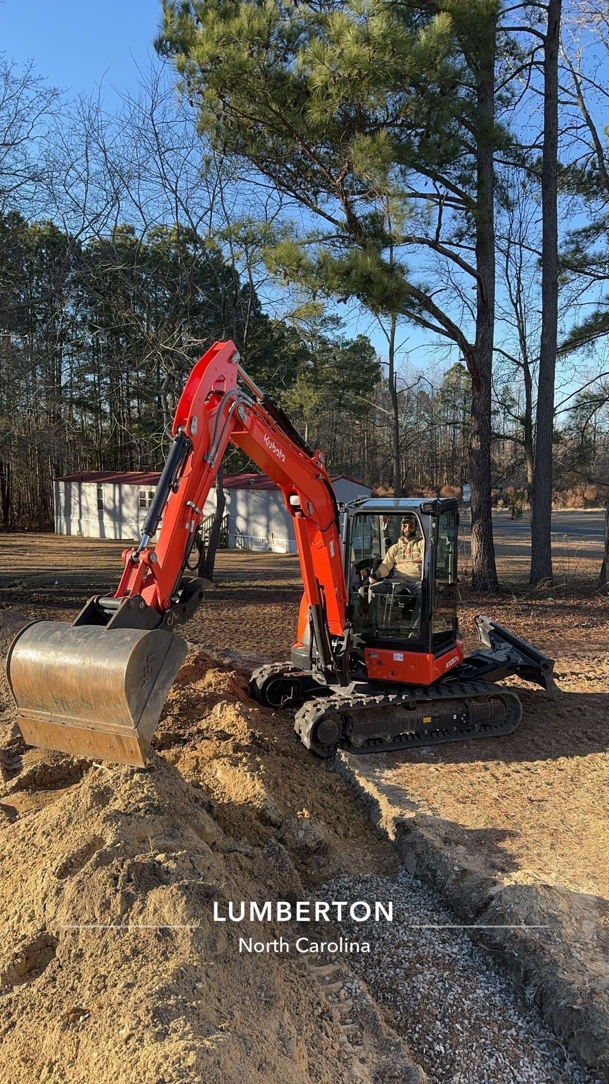 Orange Kubota excavator digging a trench outdoors on a sunny day.