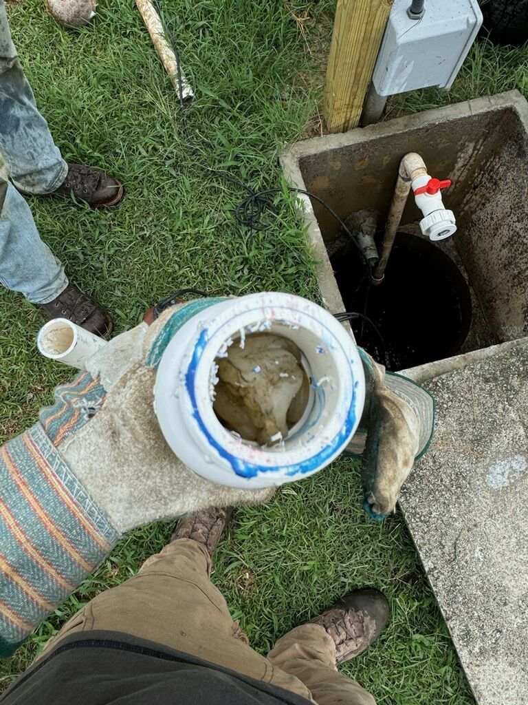 Person holding a plastic container with sludge near an open tank, outdoors.
