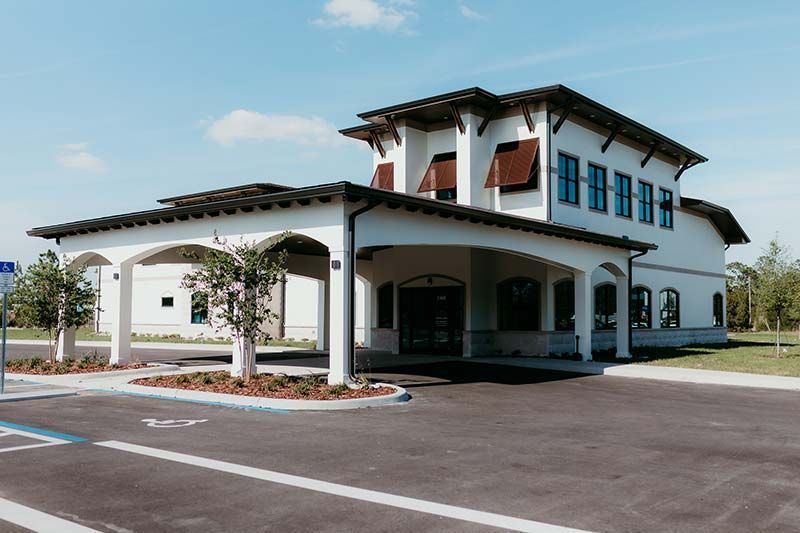 Modern white two-story building with covered entrance and parking lot under a clear sky