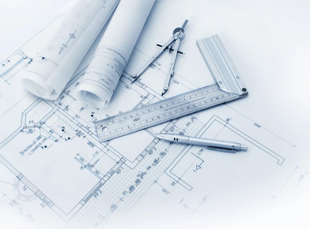 Architectural blueprints with rolled plans, drafting compass, ruler, and pencil on a white desk