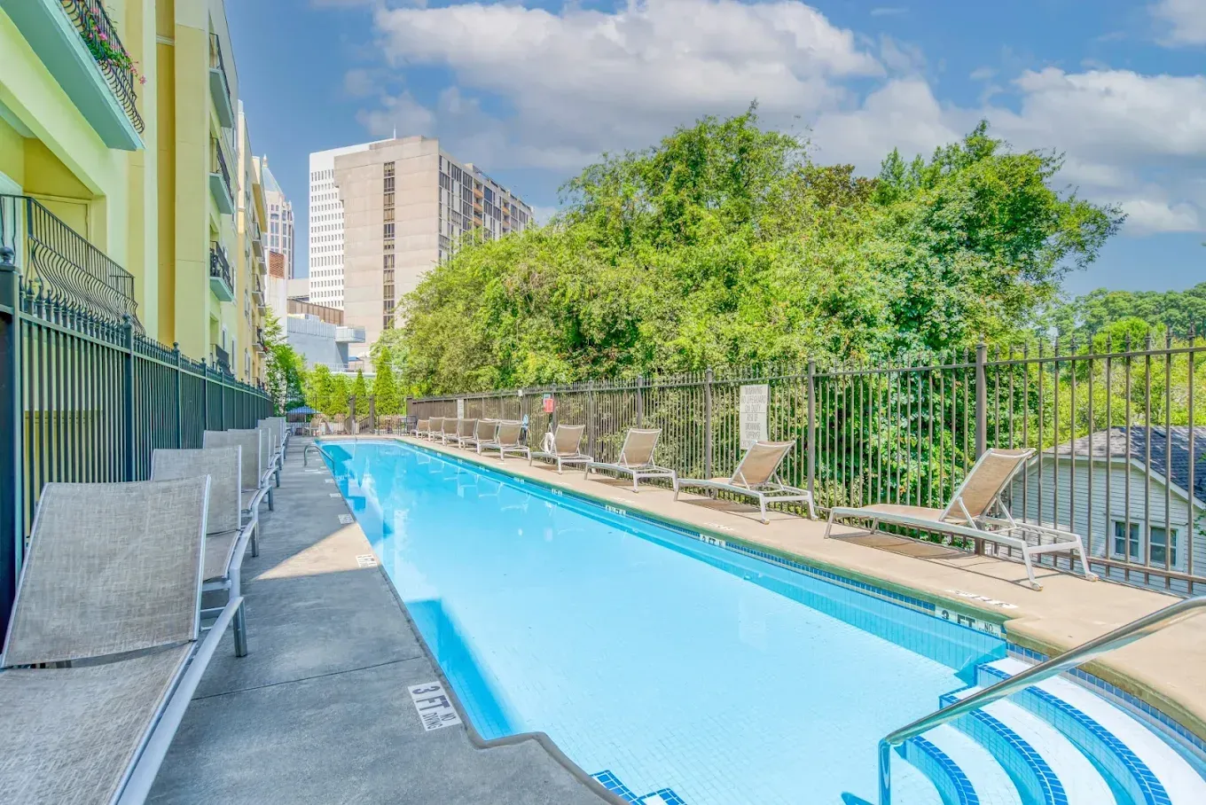 Outdoor swimming pool beside apartment buildings, with lounge chairs and lush greenery.