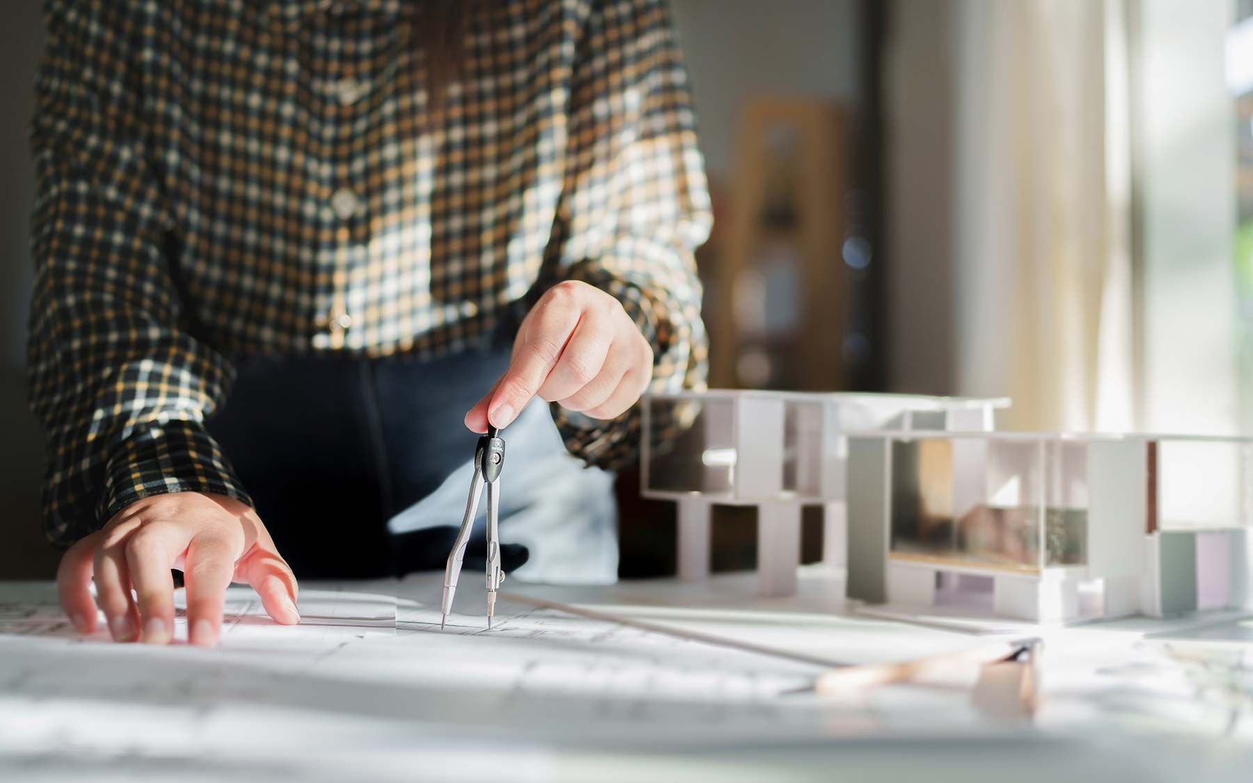 Architect reviewing blueprints with a compass on a worktable beside a small model building