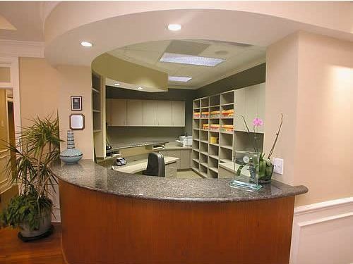 Empty reception desk with granite counter, shelves, and warm beige walls in a clinic or office lobby