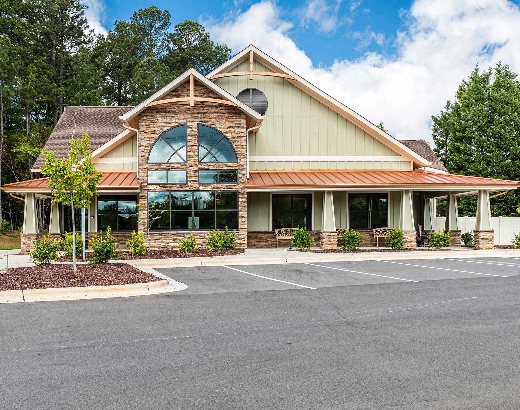 Front view of a tan-and-brown building with large arched windows and a parking lot in front