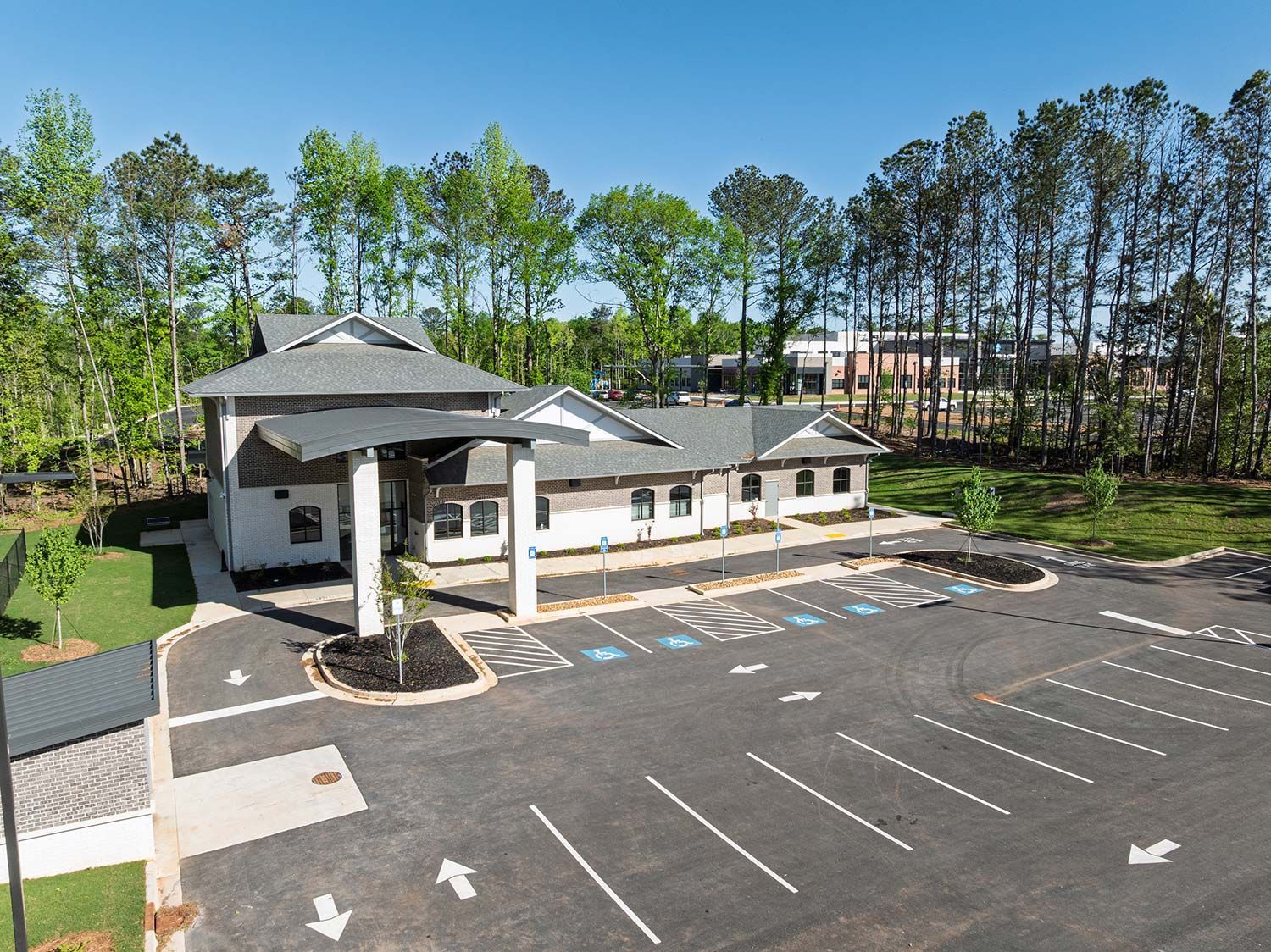 Modern building with covered entrance and empty parking lot, surrounded by trees on a sunny day