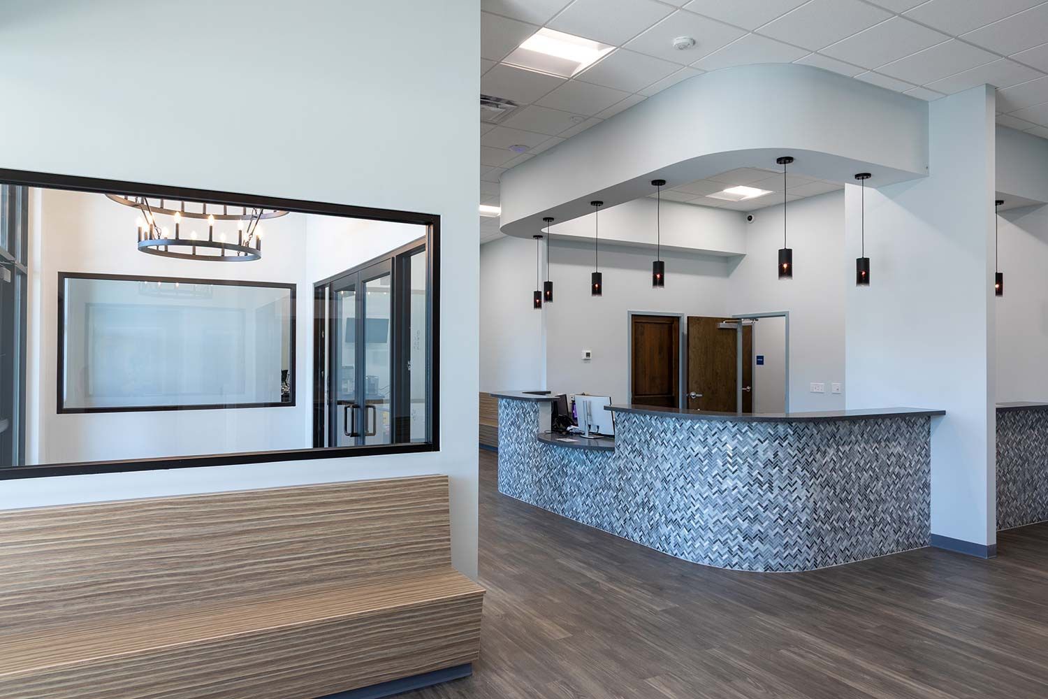 Empty modern lobby with marble reception desk, wood flooring, and large wall mirror.