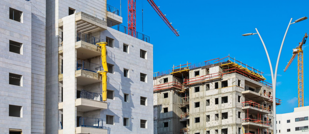 Construction site with two partially built apartment buildings and several cranes under a blue sky