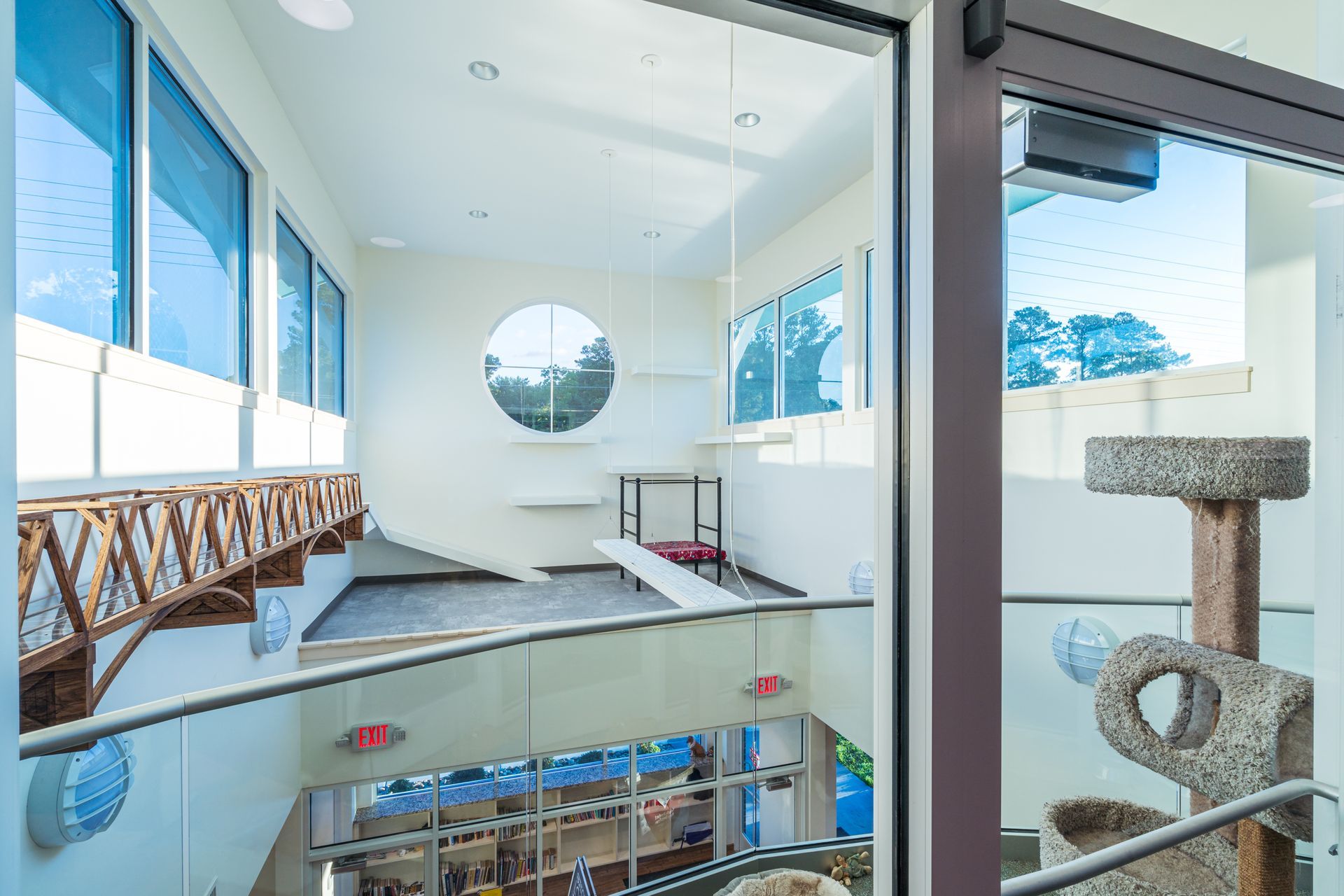 Bright modern atrium with glass walls, a bridge walkway, and a circular wall mirror above a lower level.