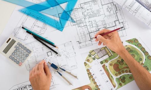 Architect reviewing house blueprints with a pencil, ruler, and drafting tools on a desk.