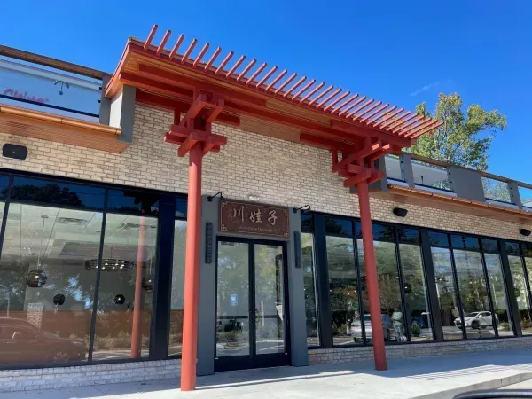 Modern storefront with red pergola entrance and large glass windows under a clear blue sky