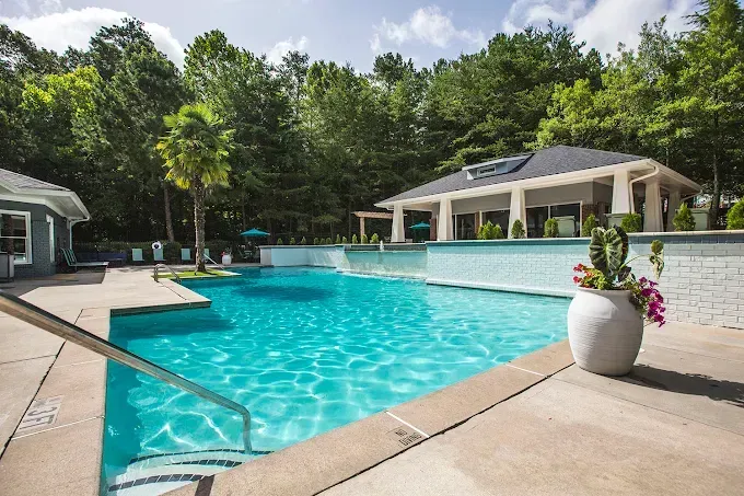 Sunny outdoor pool with turquoise water, lounge area, and a gazebo surrounded by trees