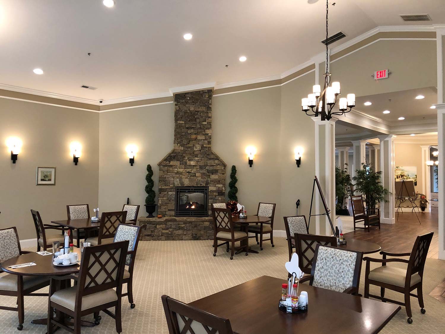 Empty dining room with tables, chairs, stone fireplace, and chandeliers under soft lighting
