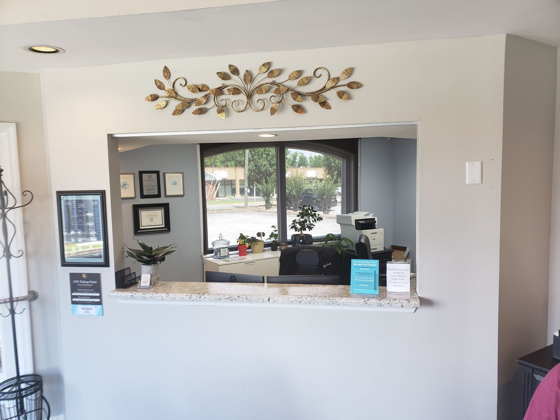 Reception window with granite counter, framed wall decor, and decorative floral art above.