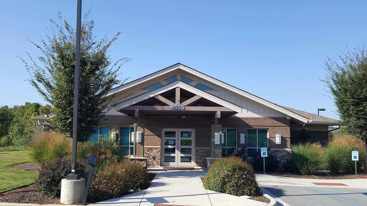 Brick community building entrance with teal doors, peaked roof, and shrubs in front