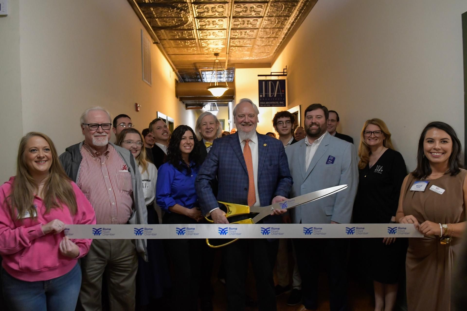 Ribbon-cutting ceremony with smiling group in a hallway, holding a commemorative ribbon.