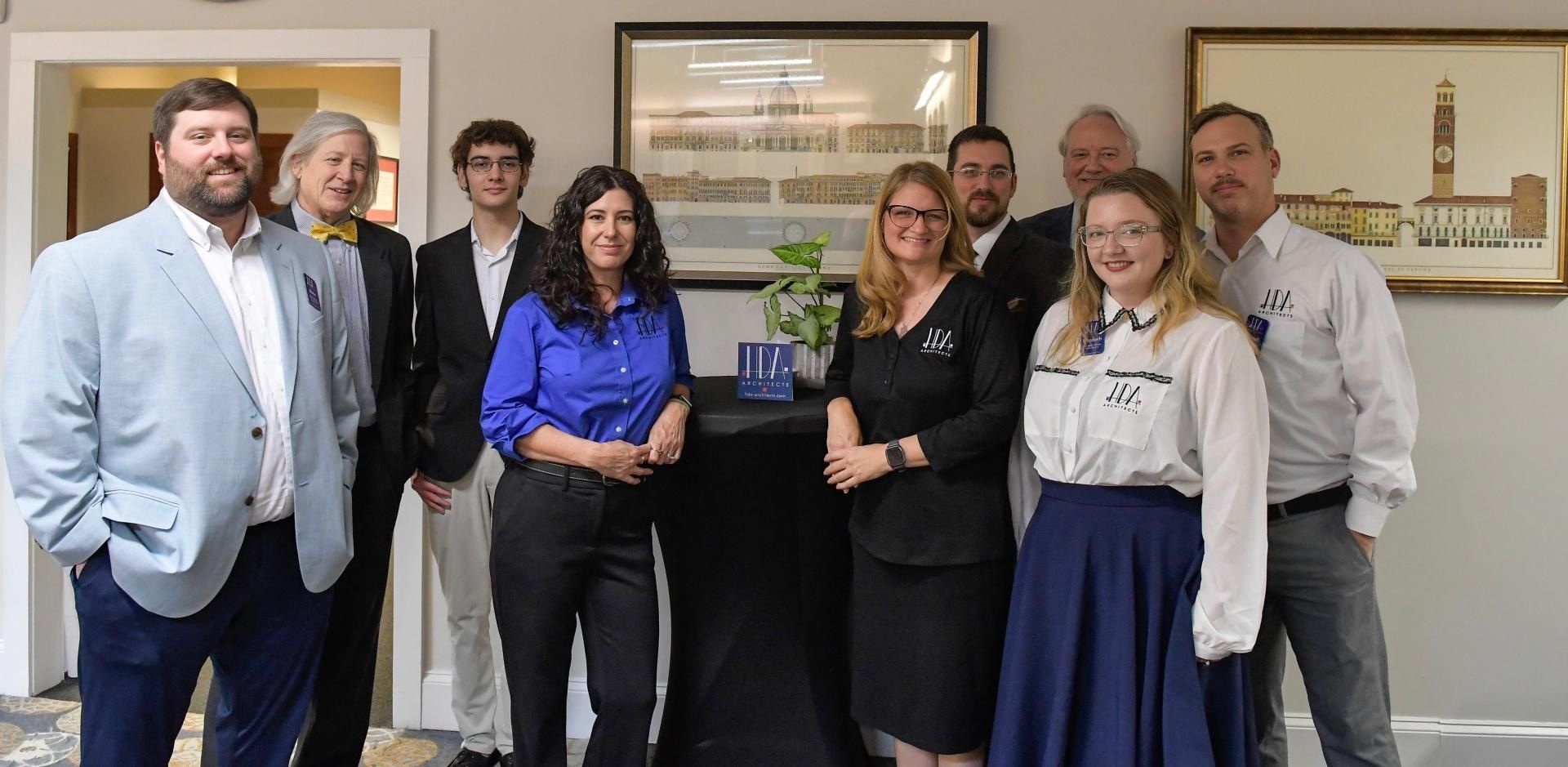 Group of people posing indoors in business attire, holding an award plaque in an office lobby.
