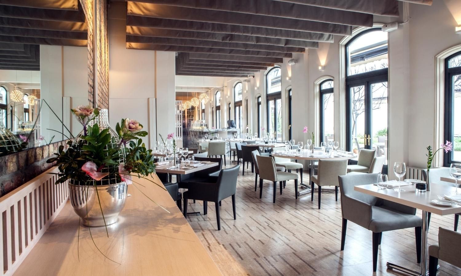 Bright modern restaurant interior with wooden tables, white columns, and floral centerpiece on the counter