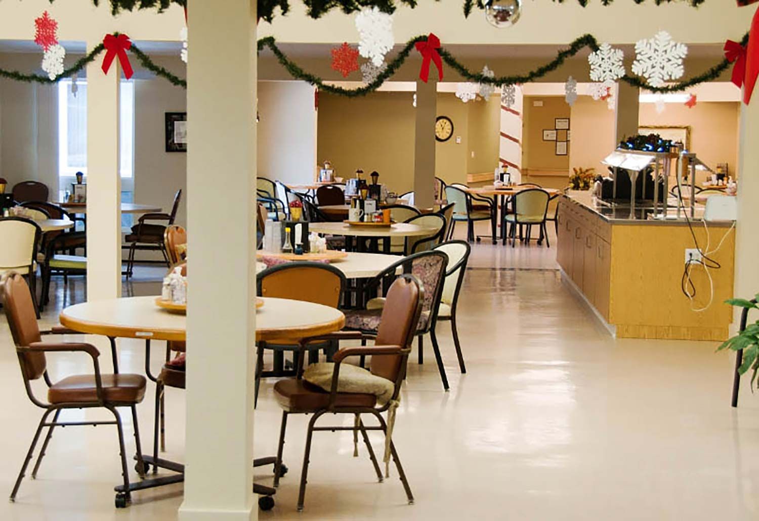 Empty cafeteria with tables and chairs, garland decorations, and a serving counter in the background