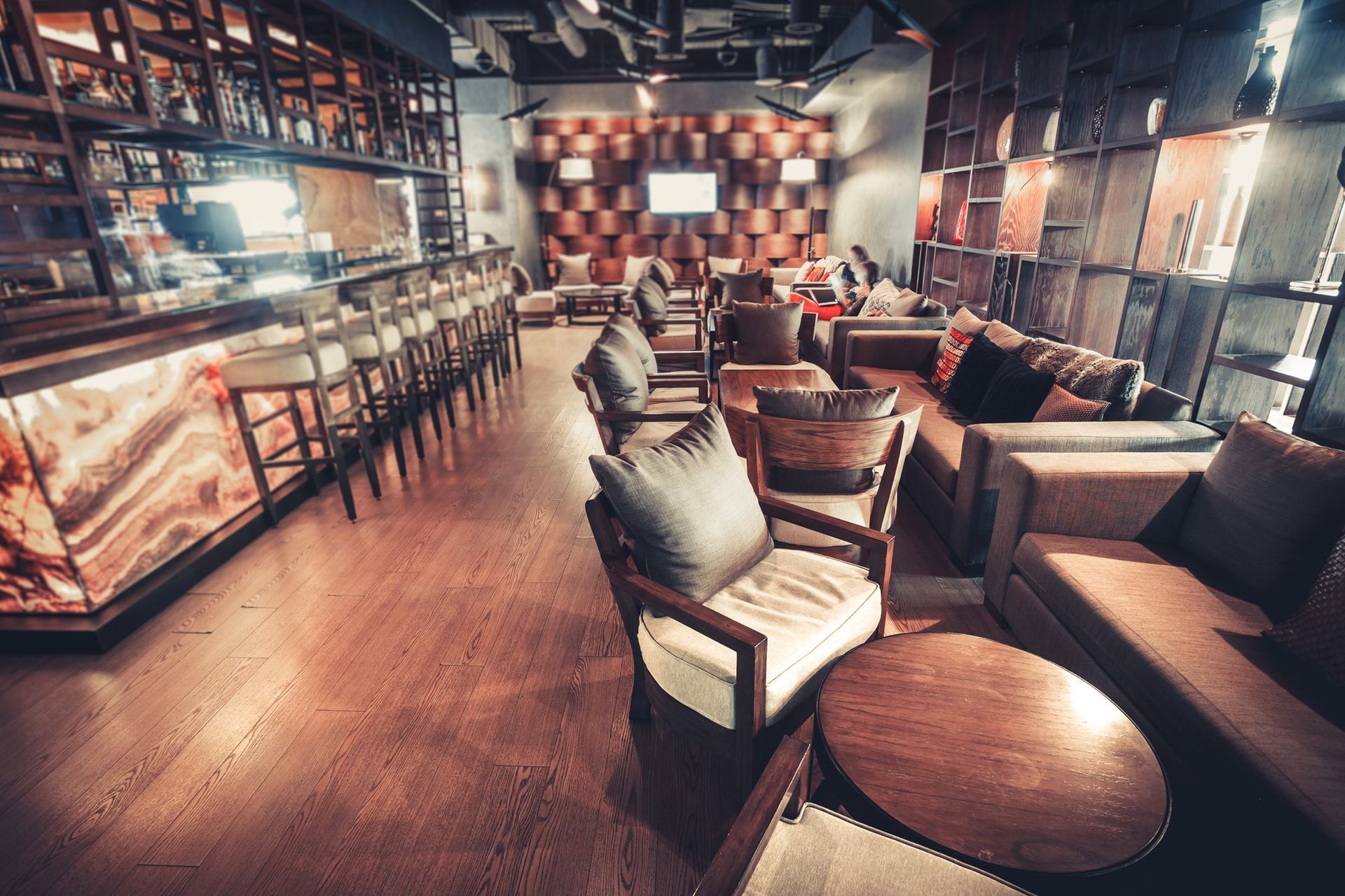 Stylish lounge with leather seating, wooden tables, and a long bar under warm ambient lighting