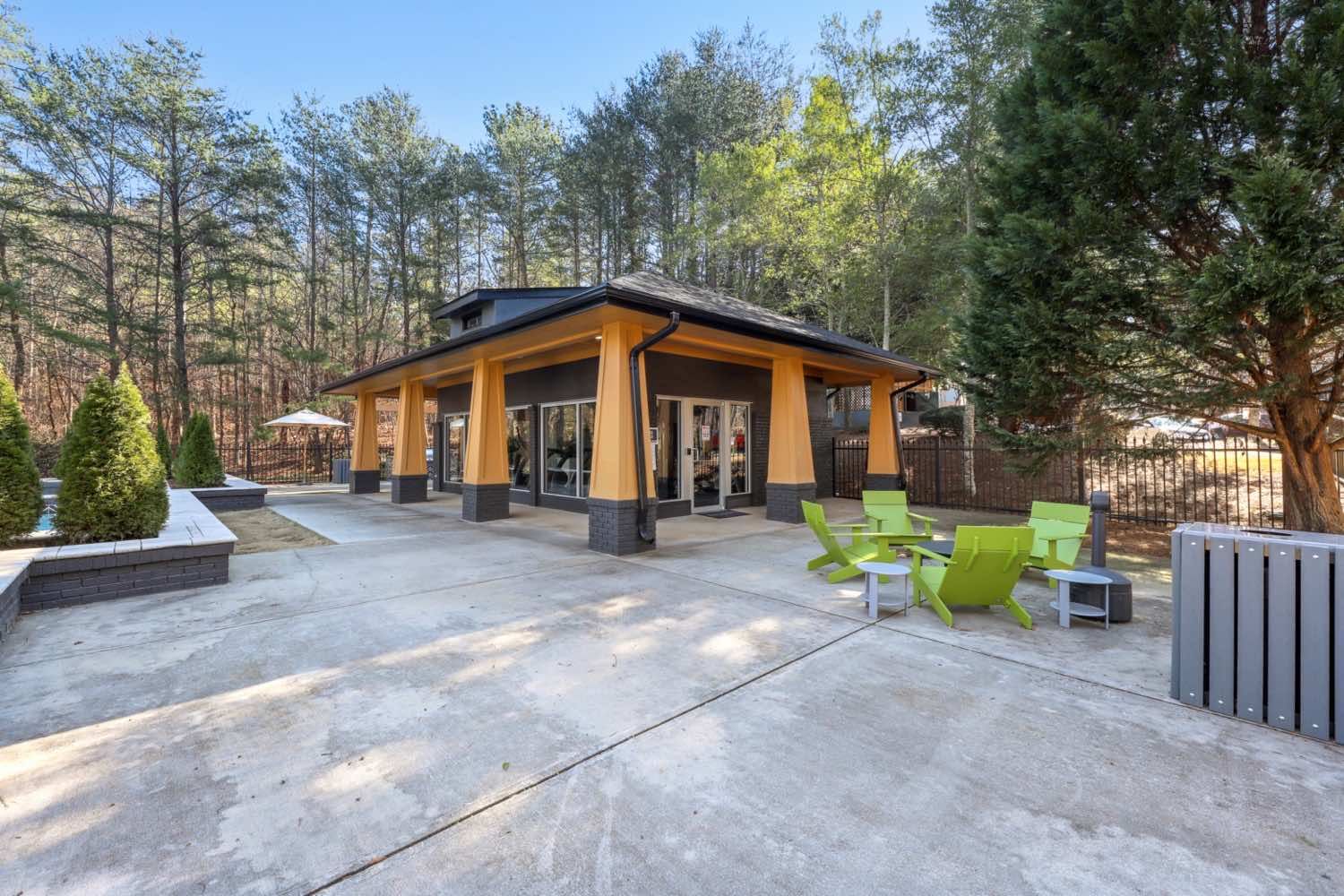 Modern outdoor patio with a pavilion, concrete seating area, and green lounge chairs surrounded by trees
