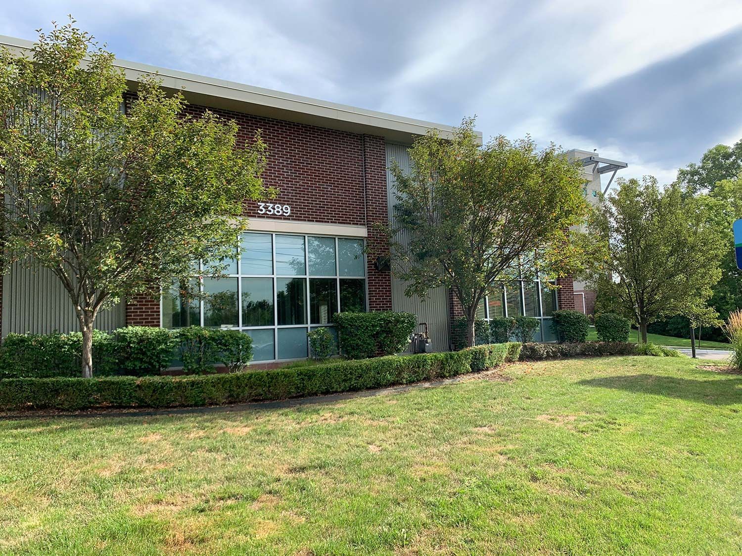 Brick office building with large windows, trees, and a green lawn under a cloudy sky