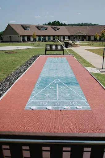 Outdoor cornhole lane with a red border and blue target board in a grassy courtyard near a building