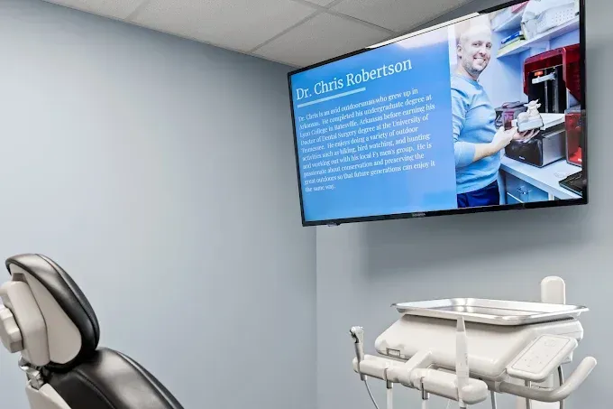 Dental exam room with wall-mounted screen showing a dentist and patient information panel