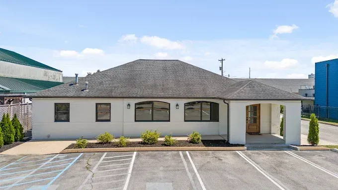 Single-story white building with gray roof, front windows, and parking spaces in front