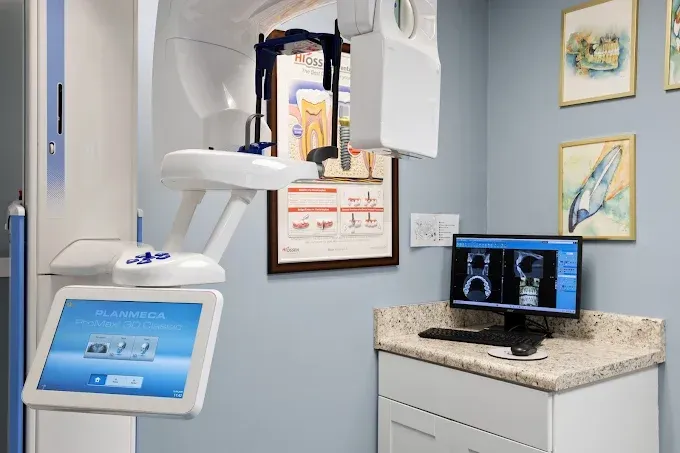 Dental office with X-ray machine and monitor beside a counter and framed wall charts
