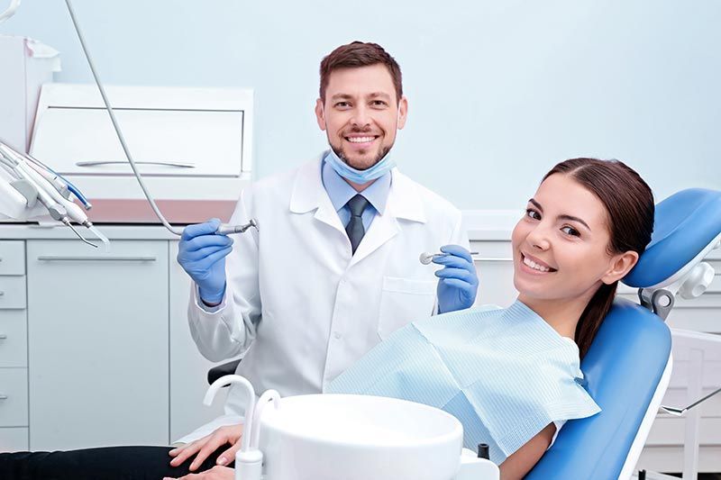 Dentist and smiling patient in a bright dental clinic with exam tools and chair