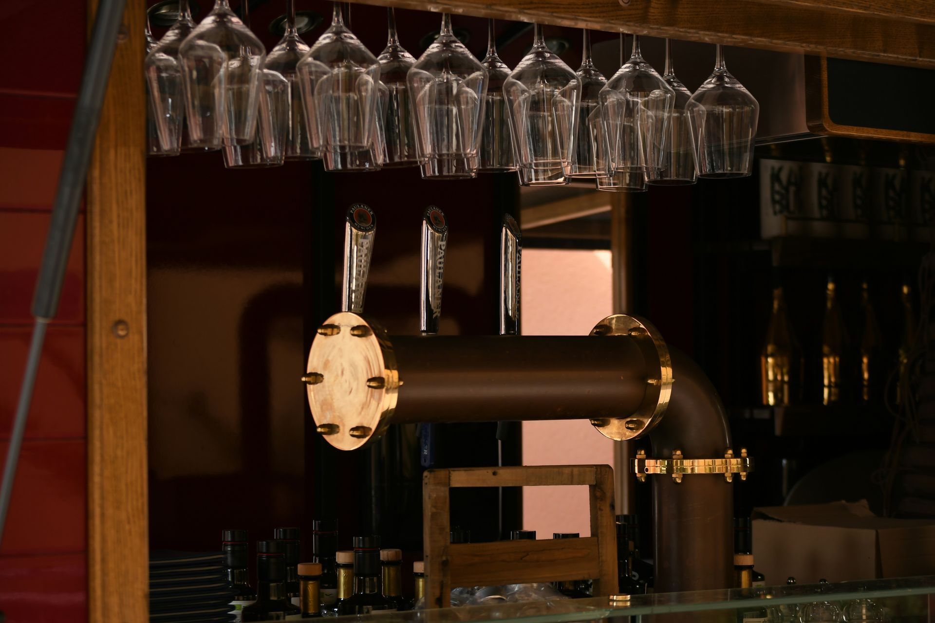 Bar with hanging wine glasses and a brass beer tap in warm dim lighting