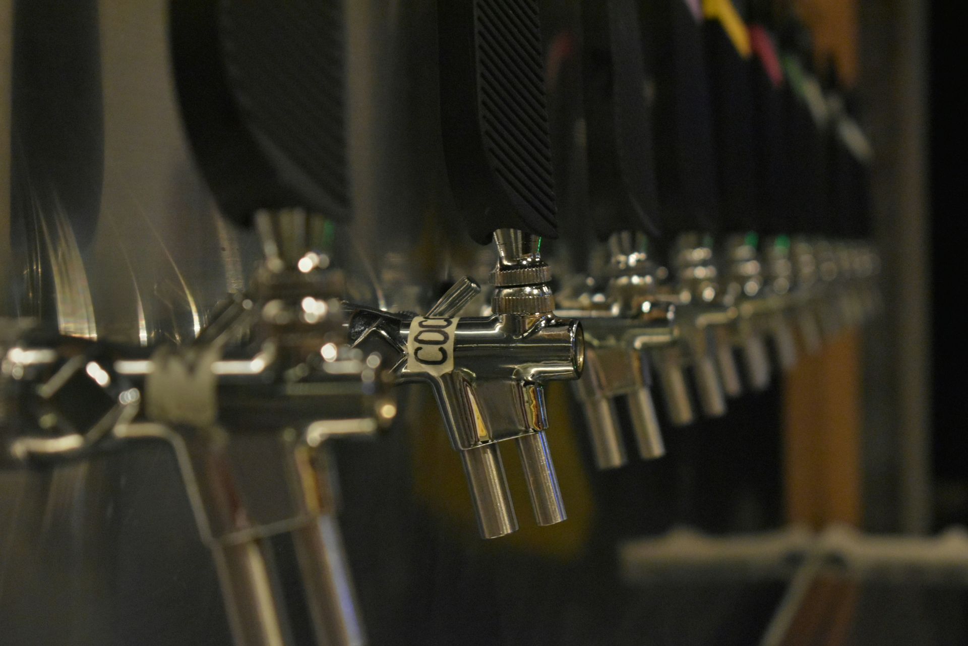 Row of beer taps on a bar counter, with metal handles and dark backgrounds