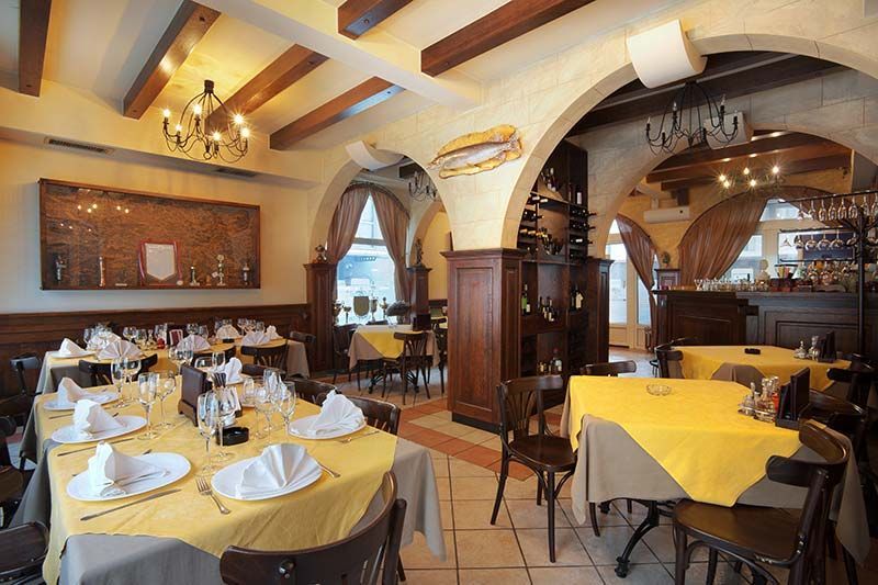 Cozy restaurant interior with yellow tablecloths, set tables, arches, and warm wooden decor