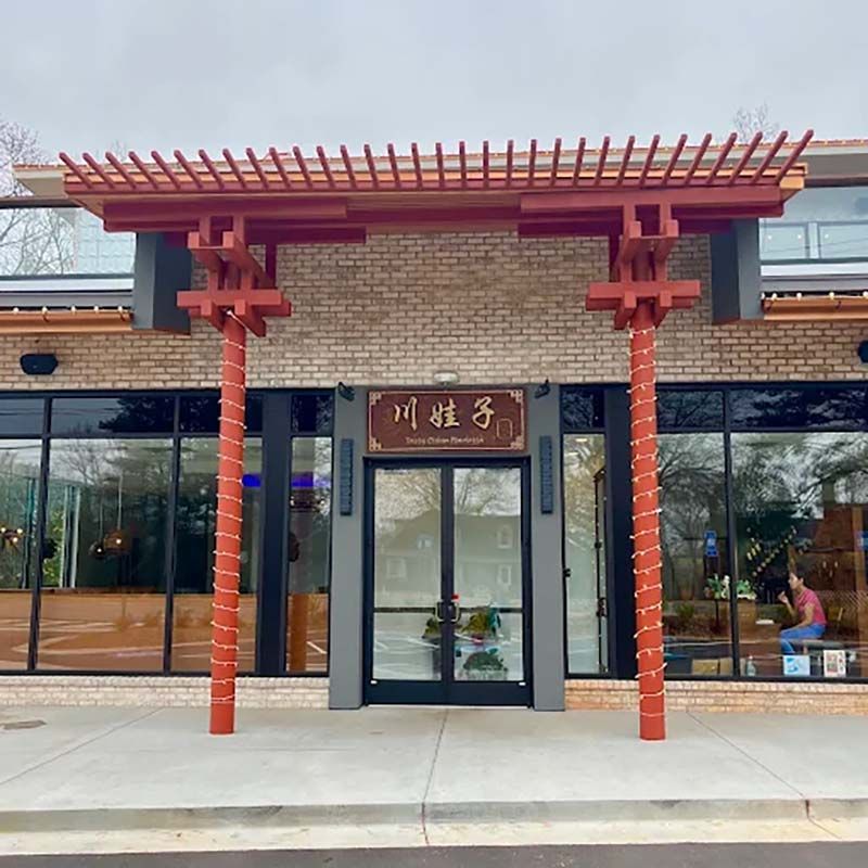 Entrance to a Chinese restaurant with a red pergola and glass doors under a brick facade.