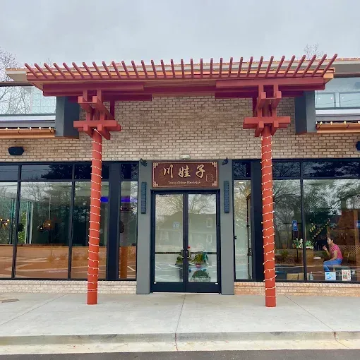 Front entrance of a building with red pergola-style columns and Chinese signage above glass doors.