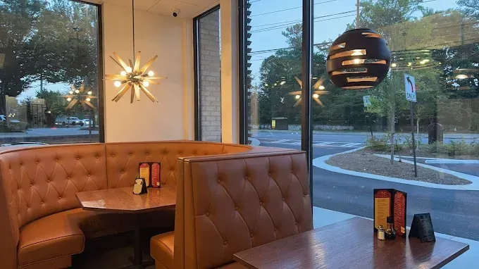 Restaurant booth seating by large windows at dusk, with warm pendant lights and tables set with menus.
