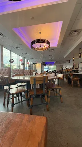 Modern restaurant dining area with tables, stools, and a purple-lit ceiling chandelier by large windows