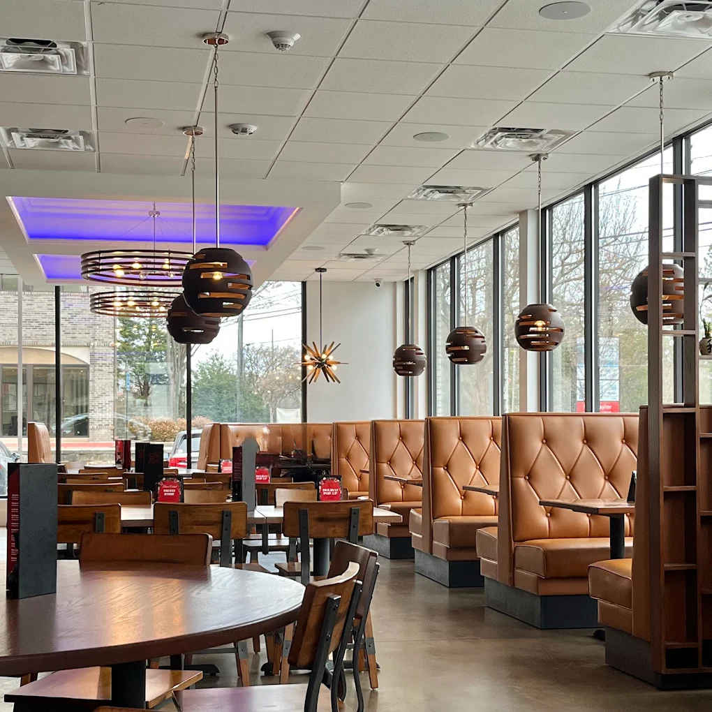 Modern restaurant interior with tan booths, round tables, and hanging globe lights by large windows