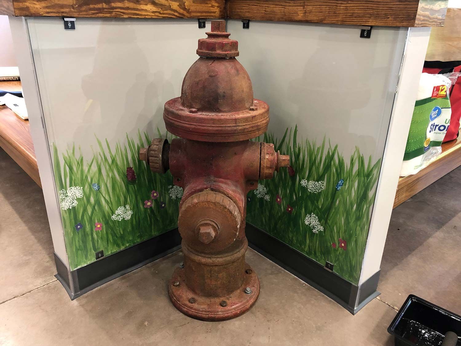 Rusty fire hydrant display in a corner with painted grass mural behind it