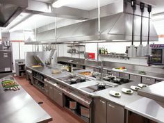 Commercial kitchen with stainless steel counters, stovetops, and overhead ventilation hoods