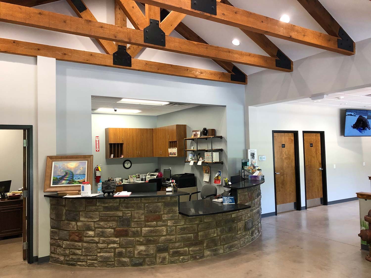 Lodge-style reception desk with stone front, wooden beams, and a service window in a bright lobby