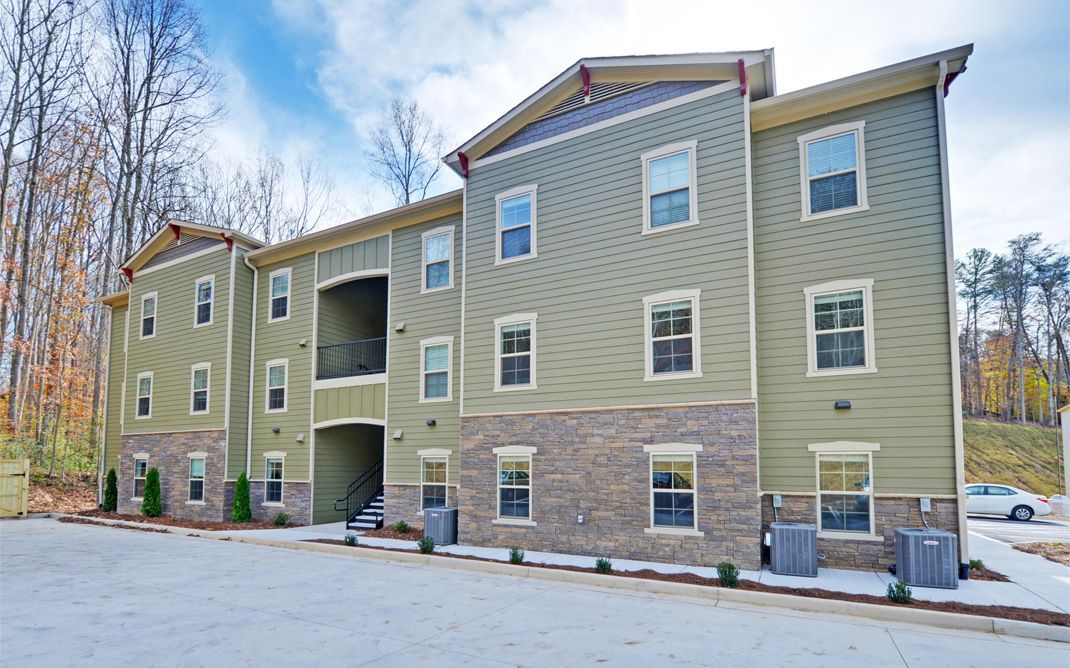 Three-story tan apartment building with stone base and snow on the ground, viewed from the parking lot