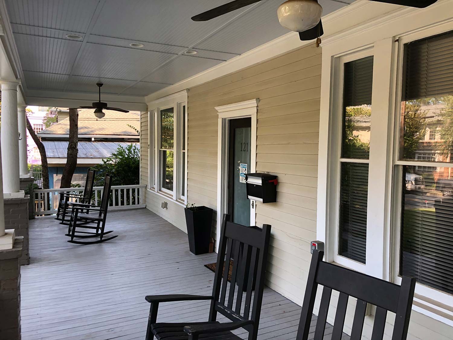 Covered front porch with white siding, black chairs, and ceiling fan overlooking a yard