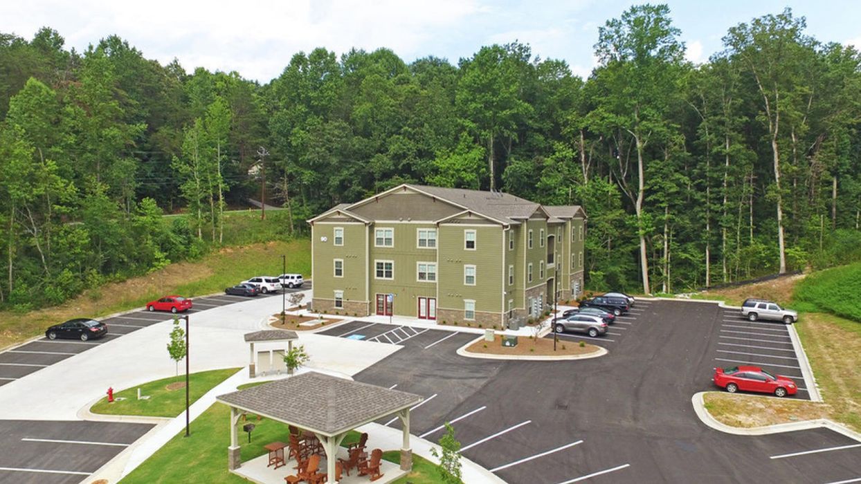 Aerial exterior view of University Loft Apartments multifamily building with parking area and wooded surroundings