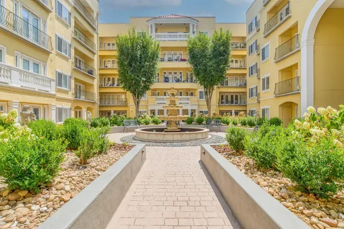 Courtyard garden walkway between yellow apartment buildings with central trees and shrubs