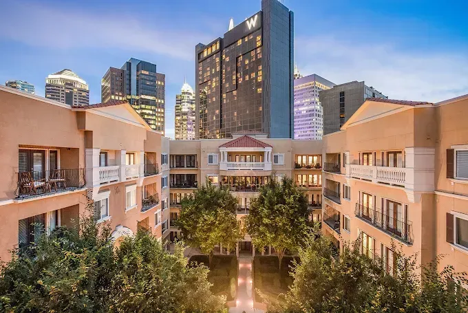 Courtyard between beige apartment buildings with trees and city skyscrapers at dusk