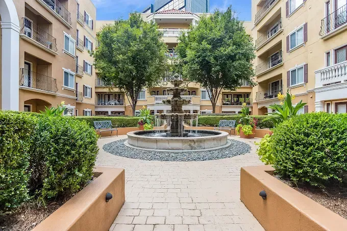 Courtyard fountain surrounded by apartment buildings, trees, and trimmed hedges.